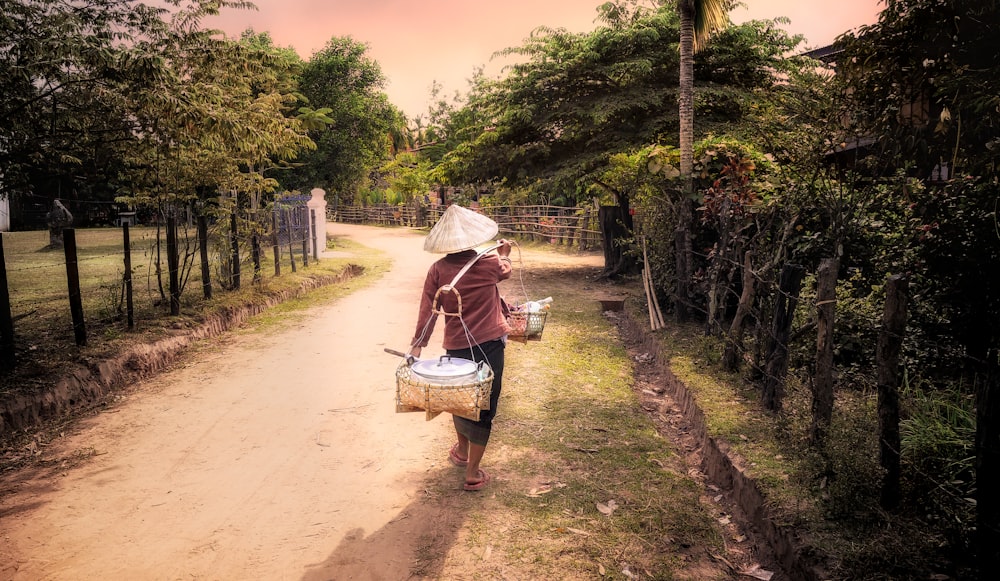 a woman walking down a dirt road carrying a basket