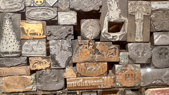 A collection of metal printing blocks with various engravings, including images of a Christmas tree, a cow, a bicycle, a lion, and several intricate designs. The blocks are densely arranged and feature both detailed illustrations and text.