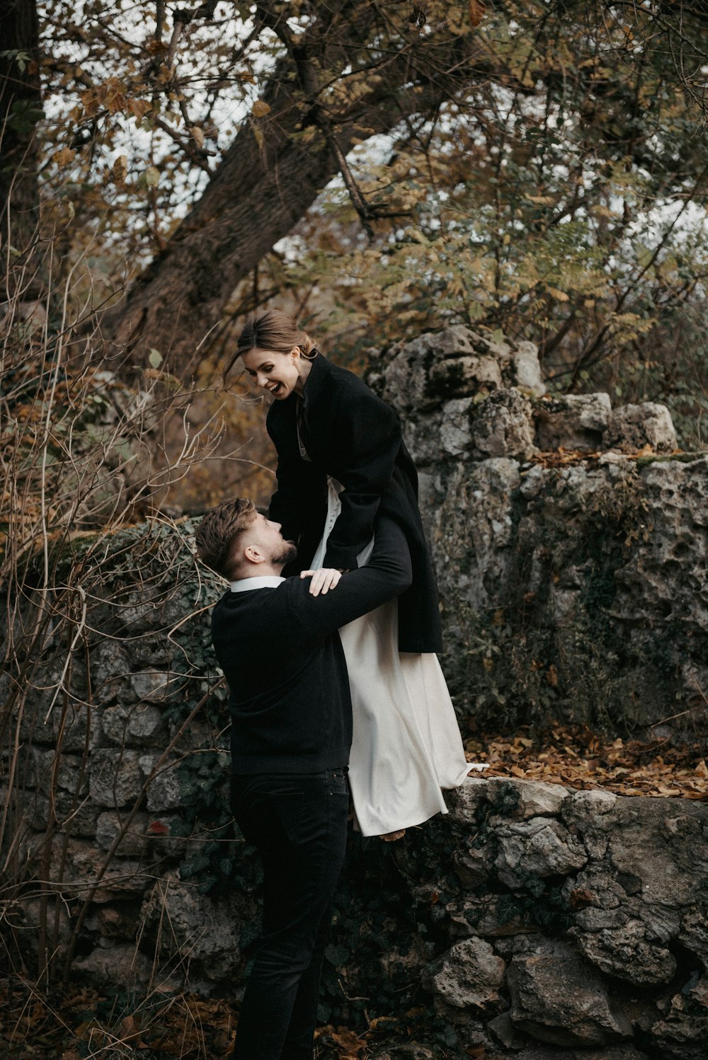a man holding a woman on top of a stone wall