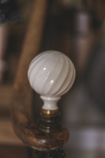 A close-up view of a decorative white ceramic knob with a spiral pattern attached to a wooden surface. The background is softly blurred, emphasizing the glossy finish of the knob and the textured wood.