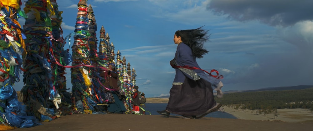 a woman in a long dress is walking by a wall of ribbons