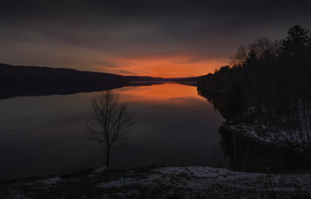 the sun is setting over a lake with trees in the foreground