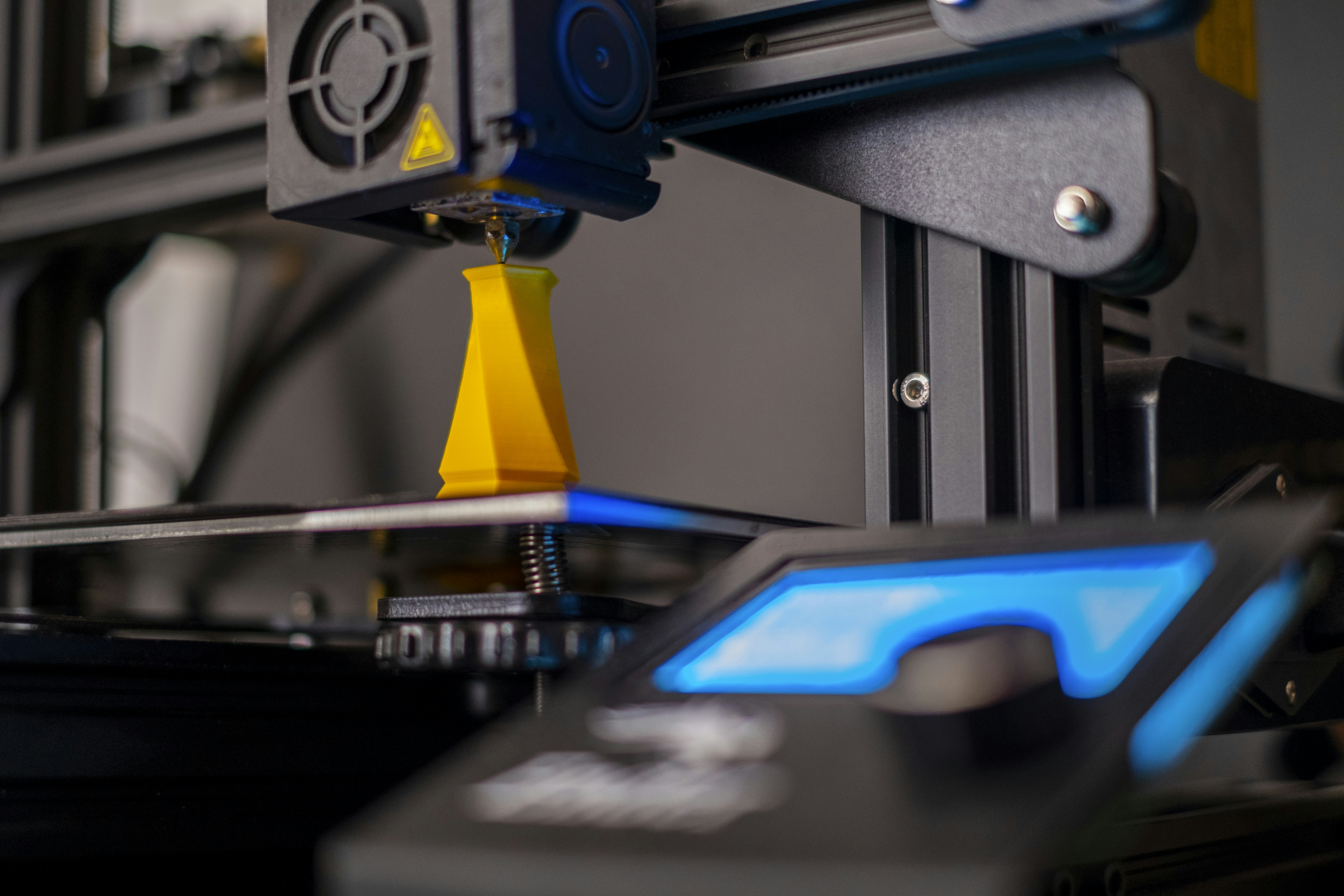 close up of 3d printer nozzle extruding blue plastic filament