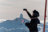 Close-up of a smiling climber taking a selfie with a mountain landscape behind.