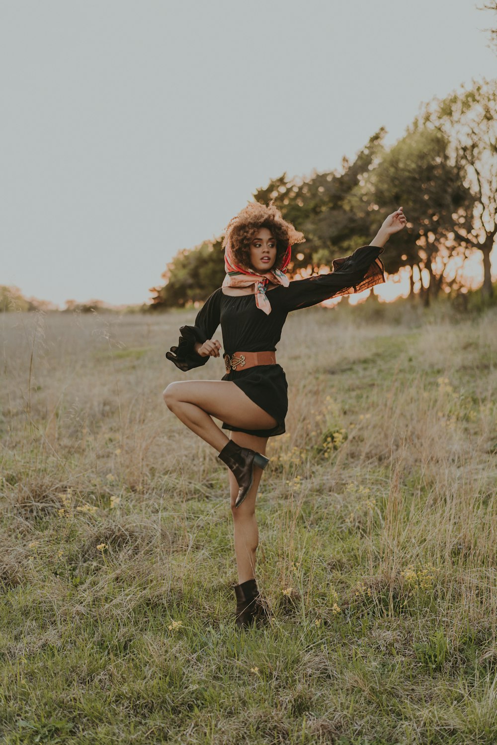a woman in a black dress is dancing in a field