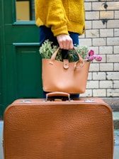 a woman carrying a brown suitcase with a plant in it