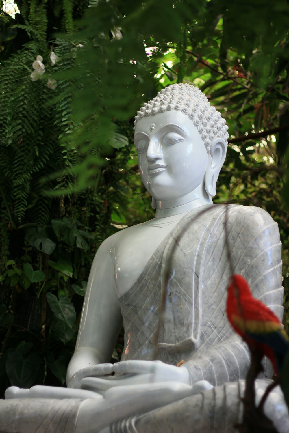 Une statue de Bouddha blanc avec un oiseau rouge assis sur ses genoux