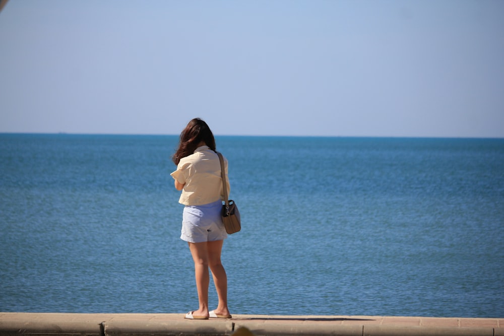 a woman standing on a ledge looking out at the ocean