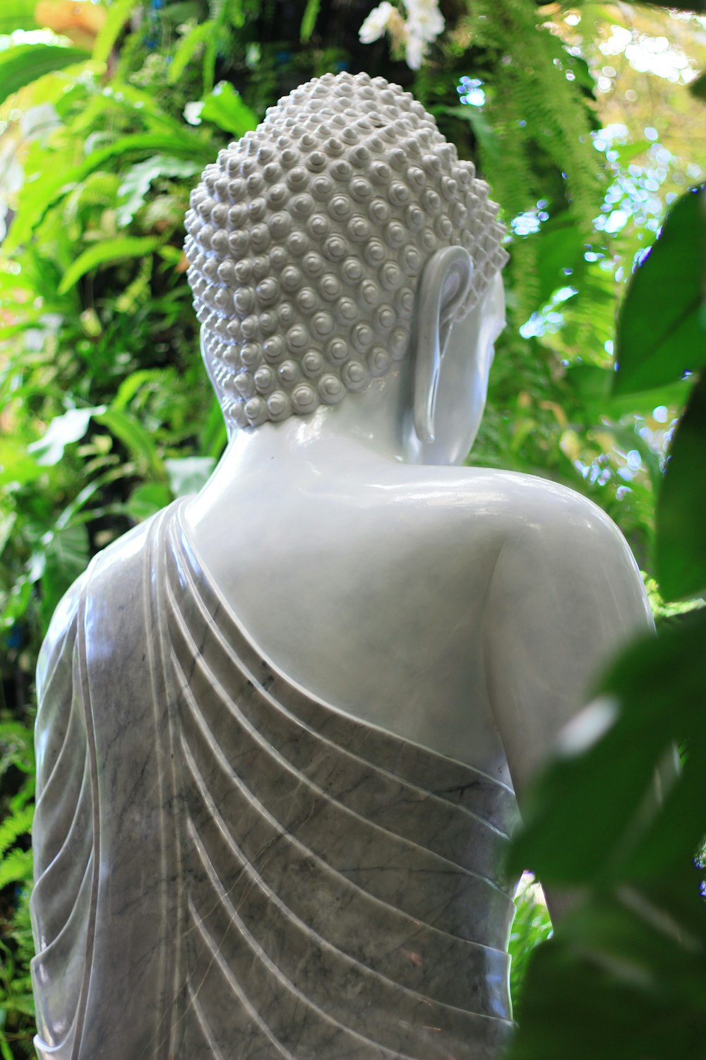 a white buddha statue sitting in front of a lush green forest