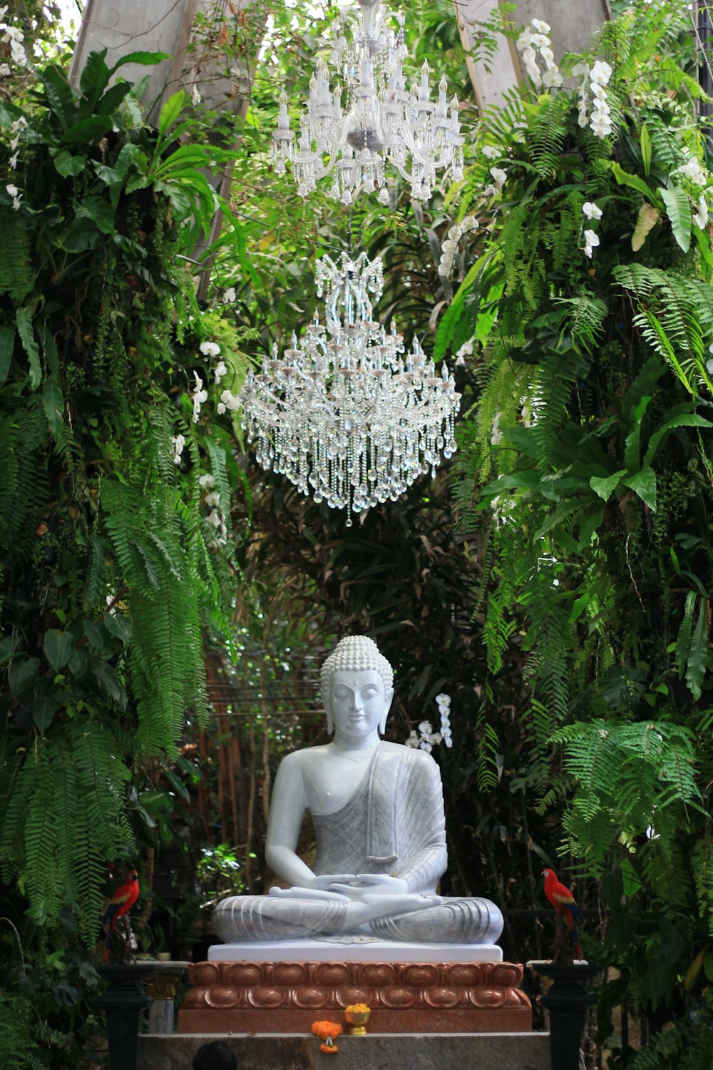 a buddha statue sitting in a garden surrounded by greenery