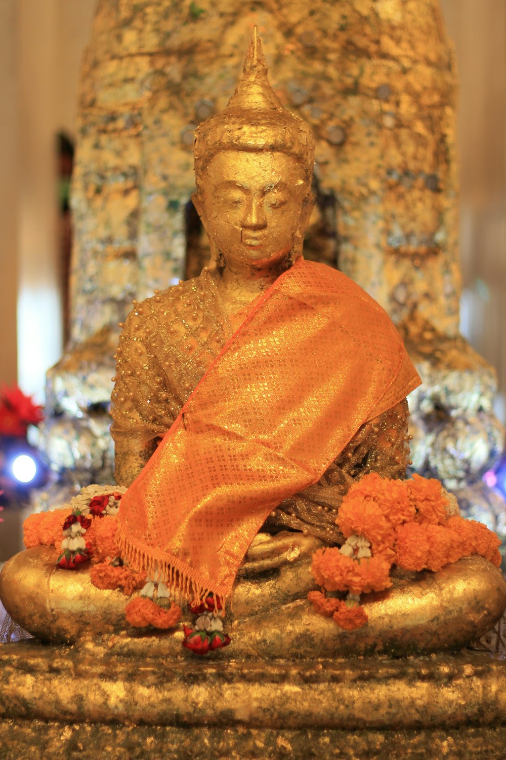 a golden buddha statue with a red scarf around it's neck