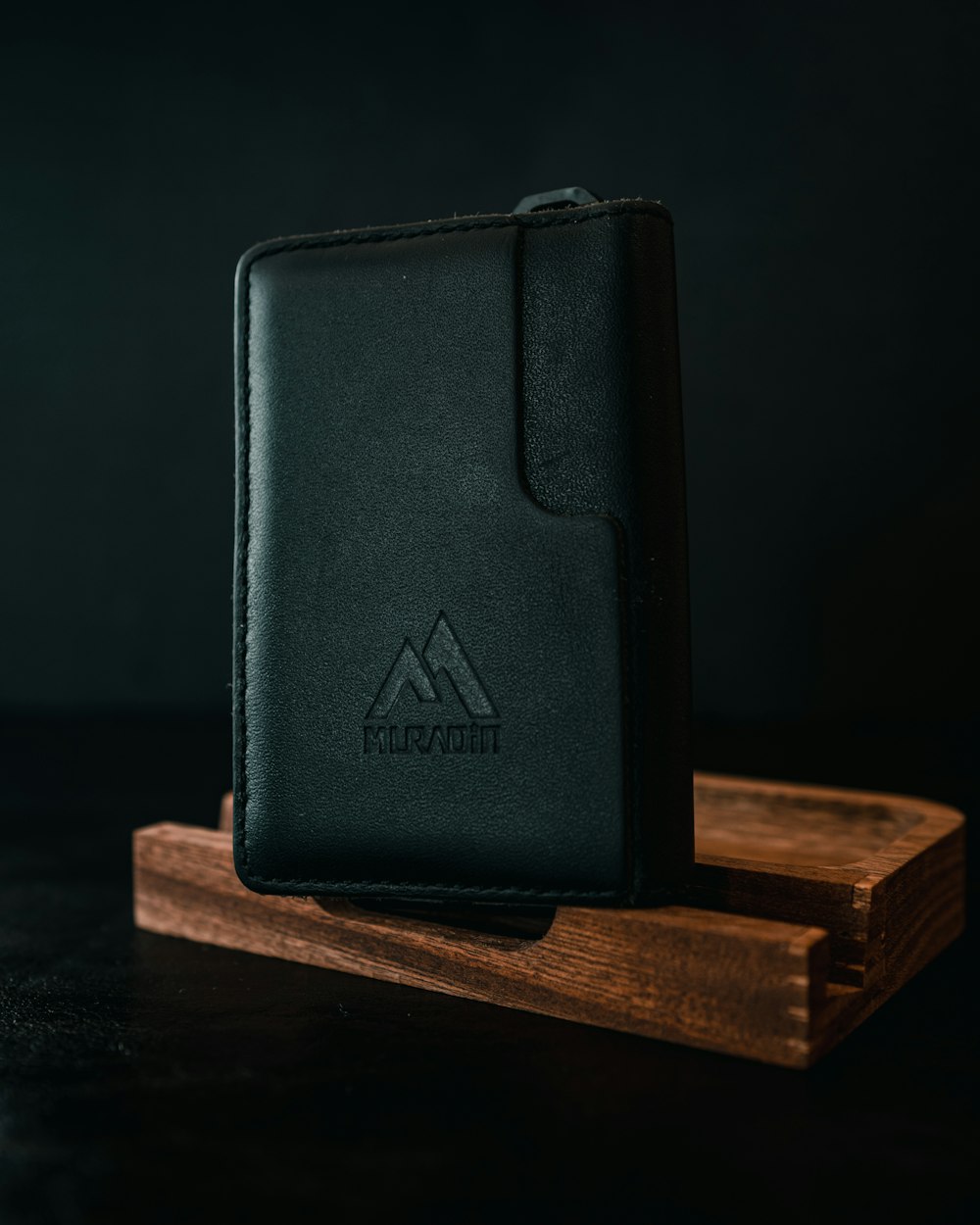 a black leather wallet sitting on top of a wooden stand