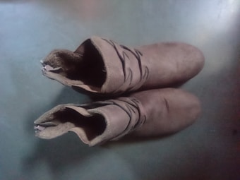 A pair of brown suede cowboy boots with decorative stitching along the upper part. The boots are positioned upright on a flat, smooth surface viewed from above.