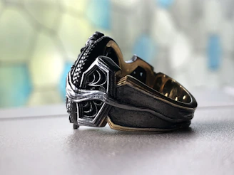 Close-up of a sleek silver ring layered with delicate chains on a marble surface.