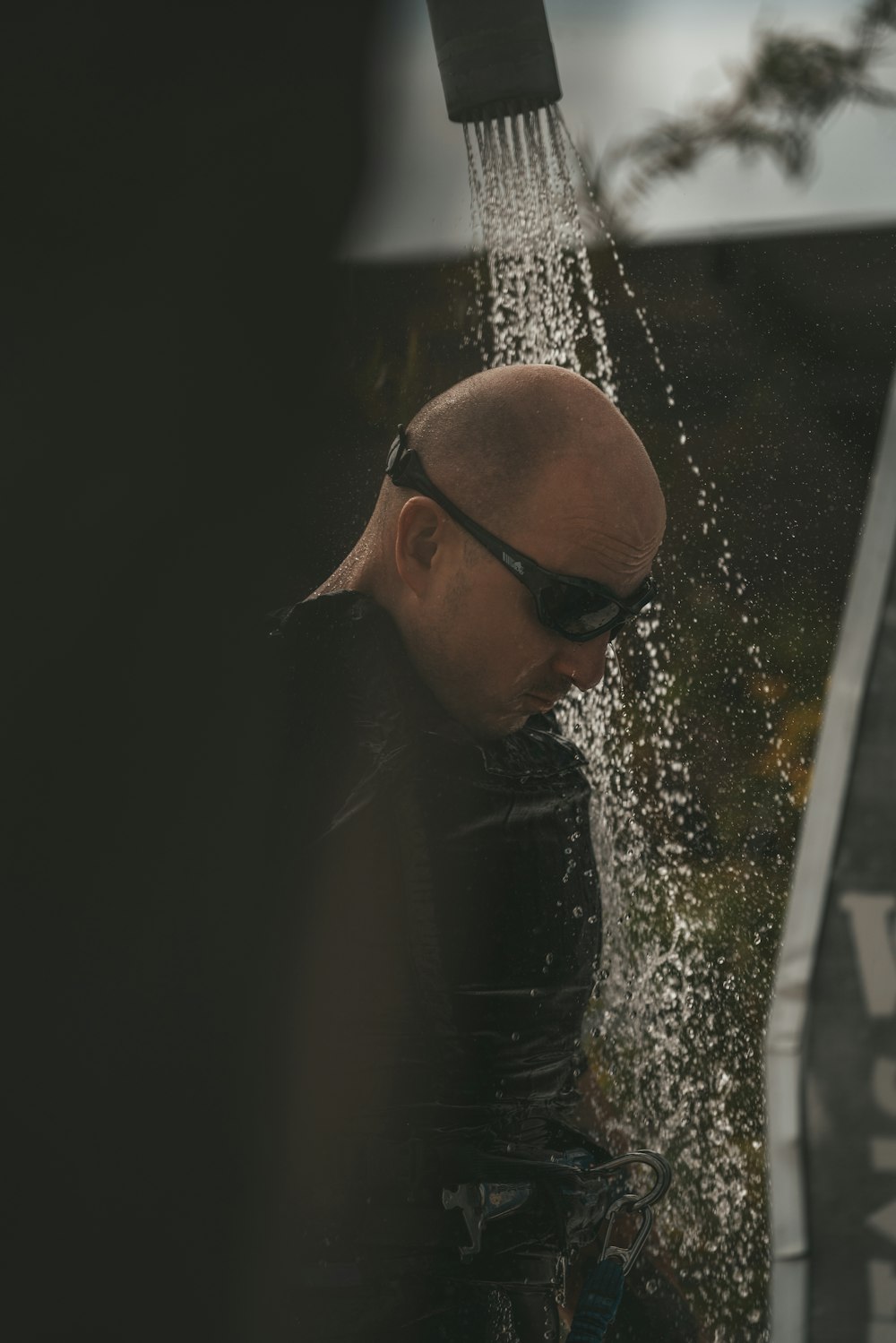 a bald man in sunglasses is spraying water from a faucet