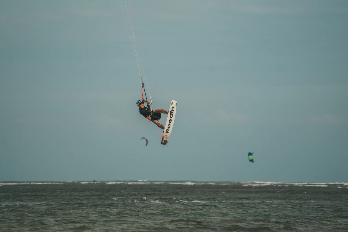 En kitesurfare högt i luften över lugnt, grågrönt vatten.
