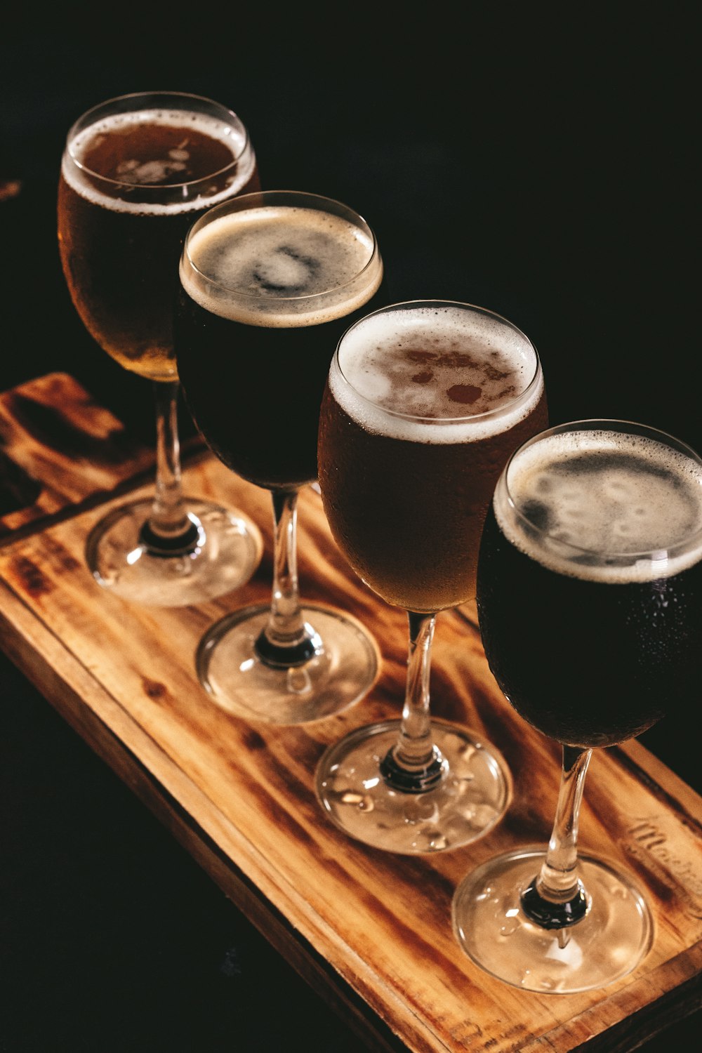 four glasses of beer sitting on a wooden tray