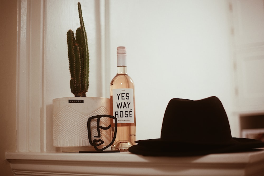 a bottle of wine and a hat sit on a mantle
