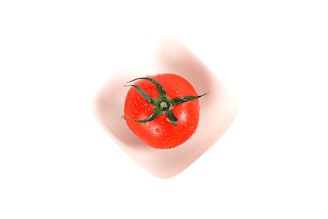 a red tomato in a white bowl on a white surface