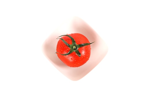 a red tomato in a white bowl on a white surface