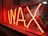 Bright red neon sign displaying the word 'WAX', set against a reflective glass surface, with a glimpse into a dimly lit room behind the sign.