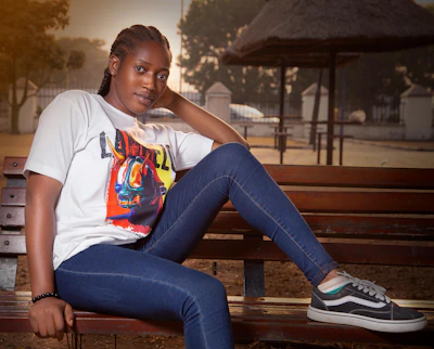 A casual outfit featuring a Perkynest t-shirt paired with jeans and sneakers on a park bench.