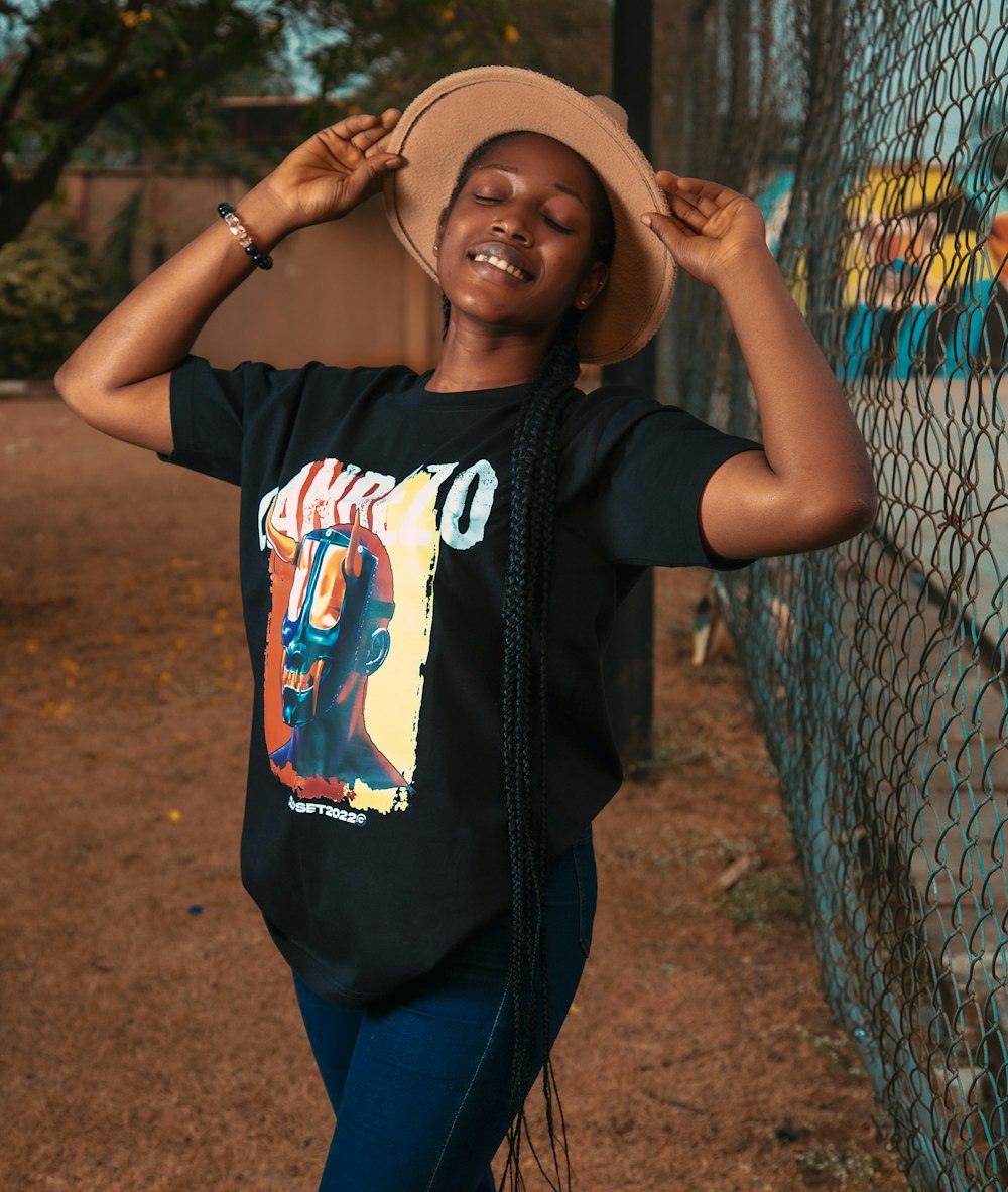 a woman leaning against a fence wearing a hat