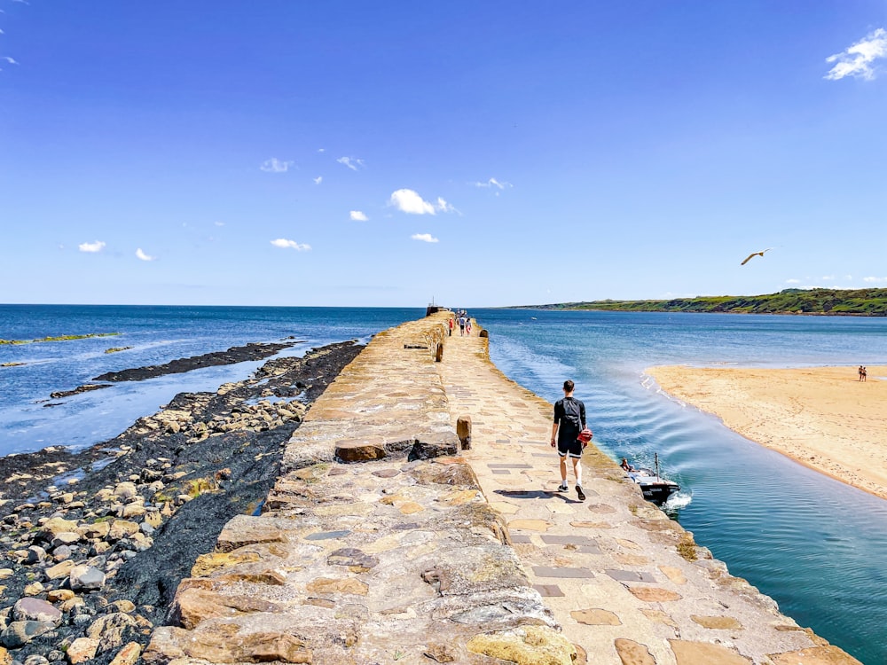 a man walking along a stone wall next to a body of water