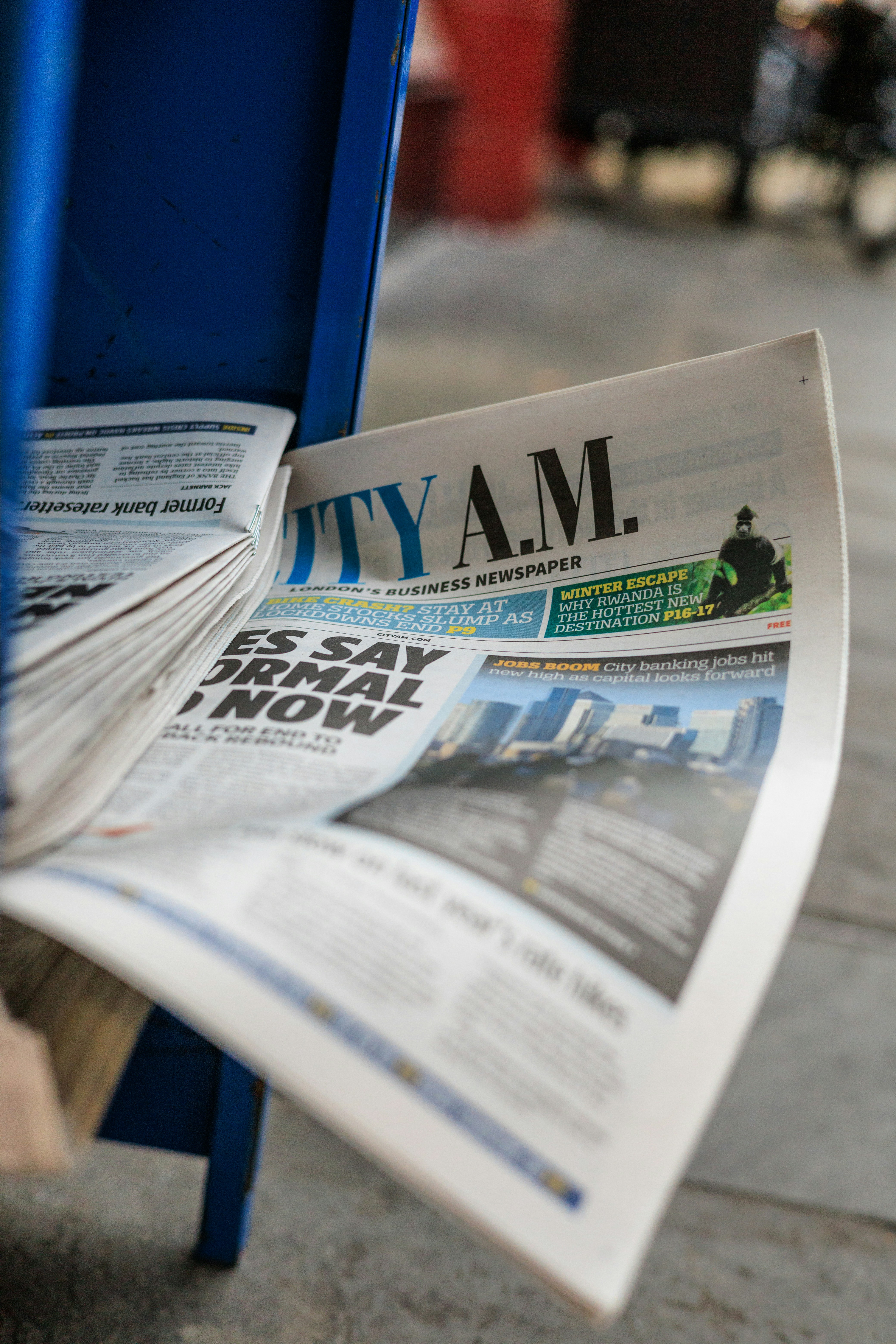 tumpukan koran yang duduk di atas tempat sampah biru