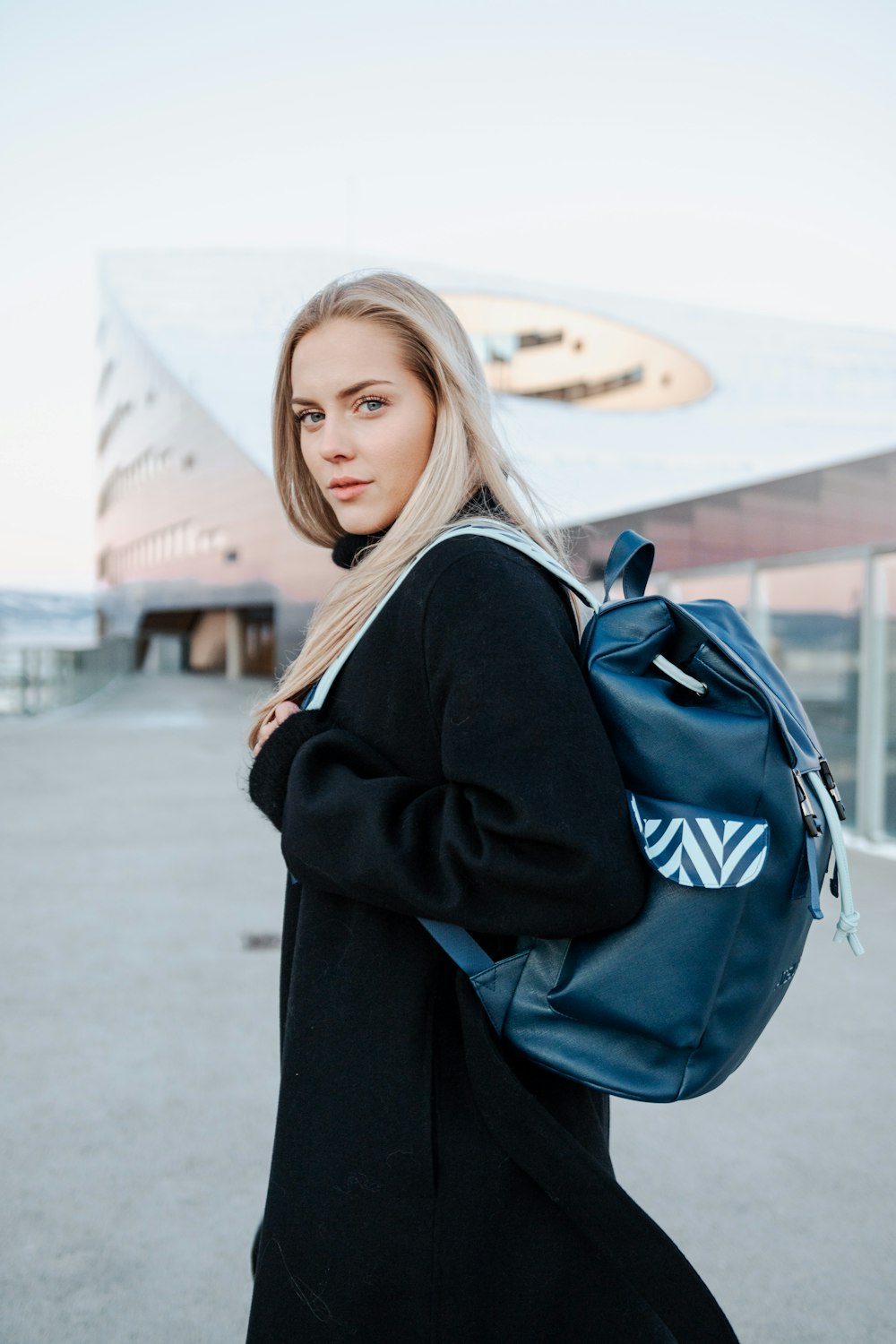 a woman in a black coat carrying a blue backpack