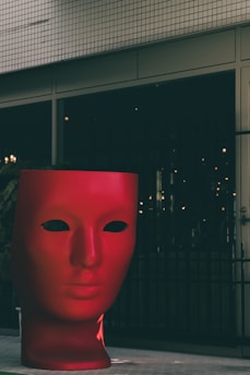 a large red mask sitting in front of a building