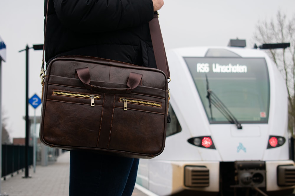 a person holding a brown briefcase in front of a train