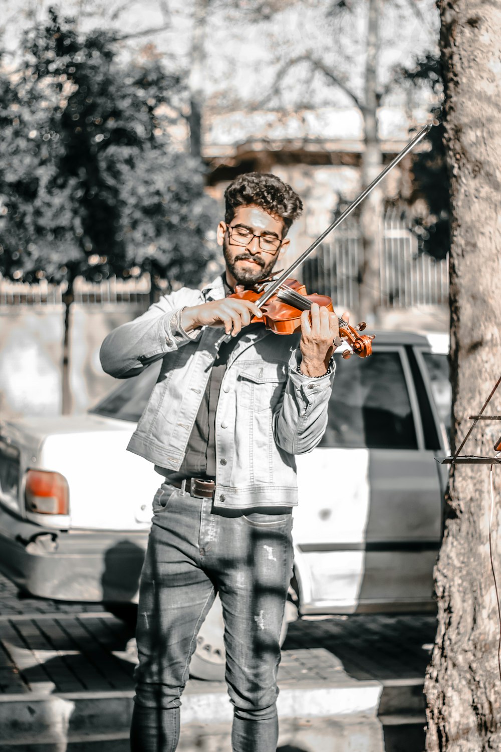 a man holding a violin while standing next to a tree