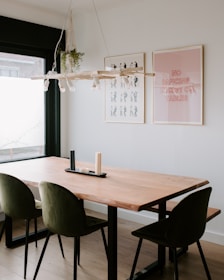 A minimalist dining table set with olive green placemats, charcoal gray dinnerware, and delicate wall art in soft sand tones.