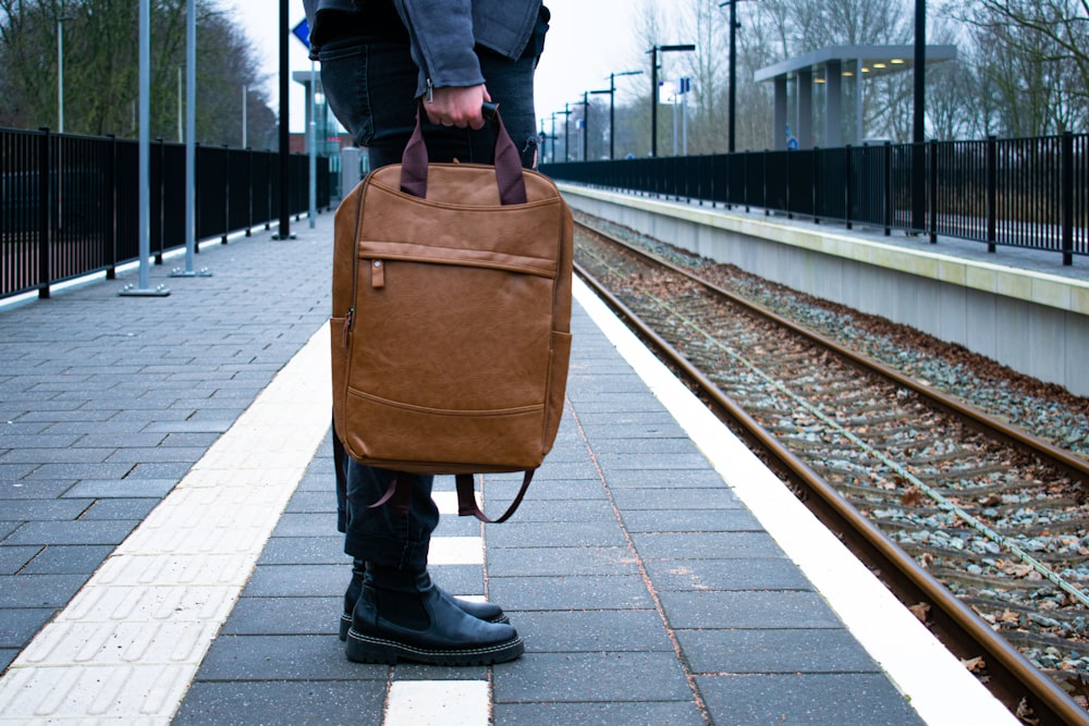 Eine Person, die eine braune Tasche auf einem Bahnsteig hält