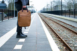 a man carrying a brown briefcase on a train track