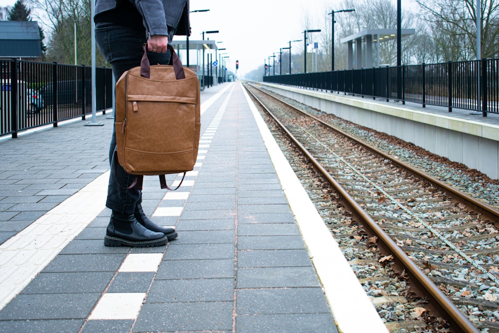 Un hombre que lleva un maletín marrón en una vía de tren
