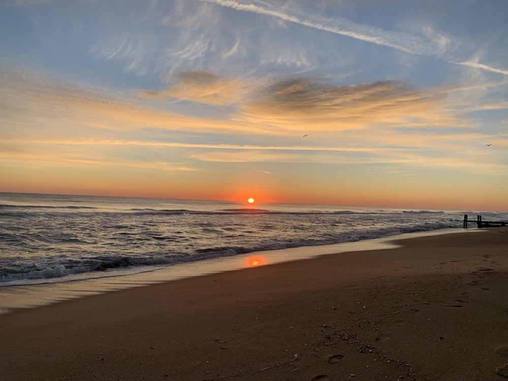 the sun is setting over the ocean on the beach