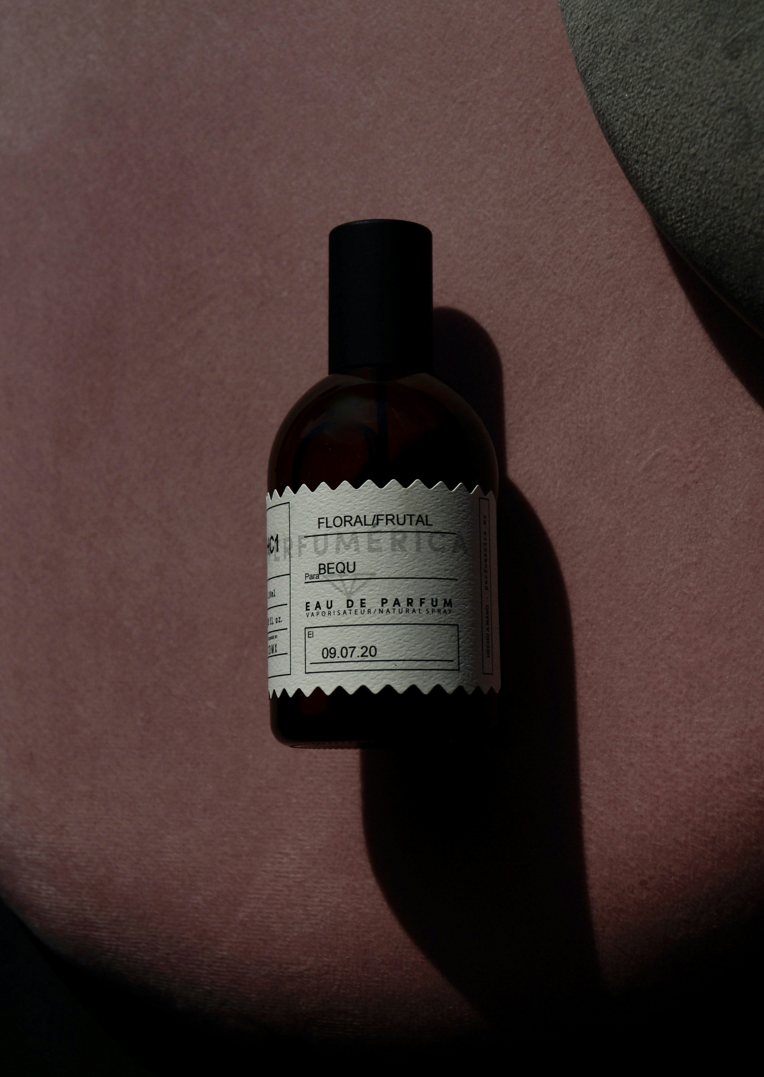 Dark rose perfume bottle with black cap on dark velvet surface