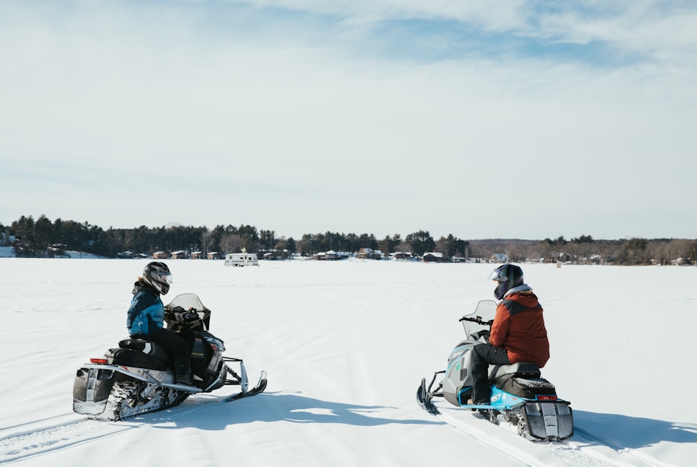 two people riding snowmobiles in the snow