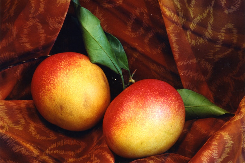 two oranges with leaves on a brown cloth