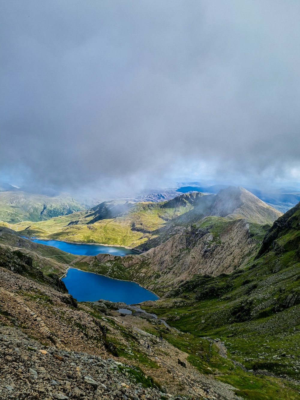 a blue lake surrounded by mountains under a cloudy sky