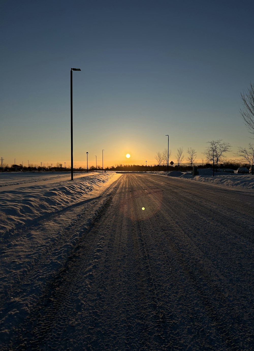 the sun is setting over a snowy road