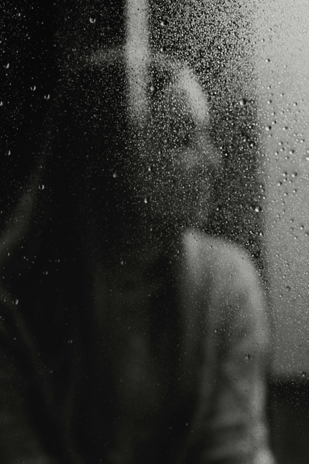 a person standing in front of a window covered in rain