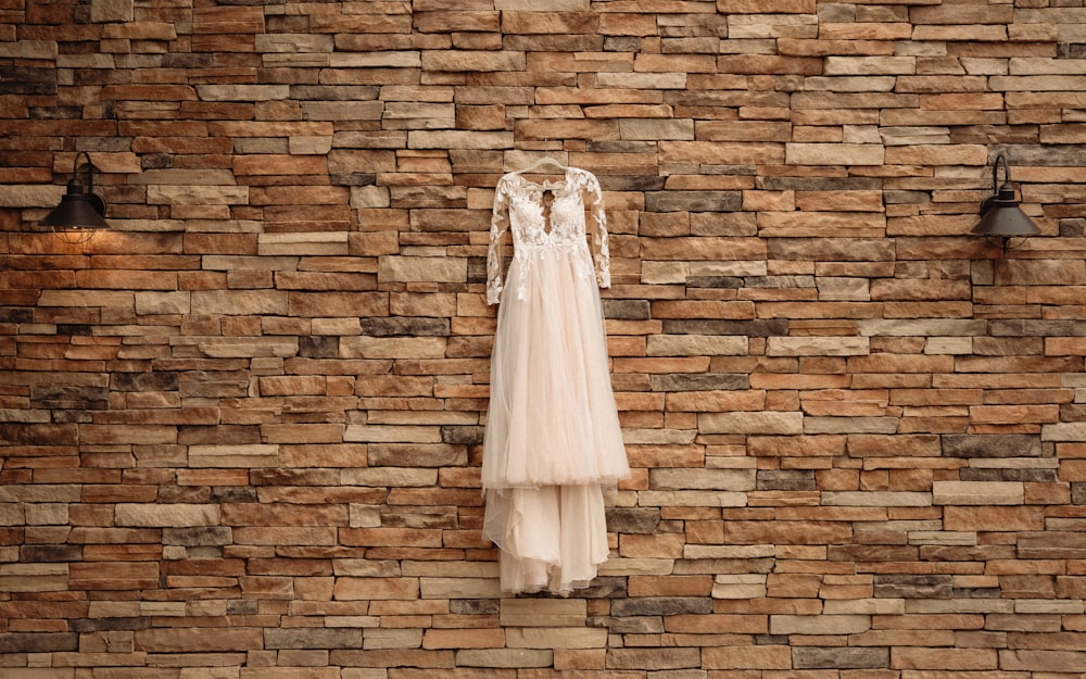 a wedding dress hanging on a brick wall