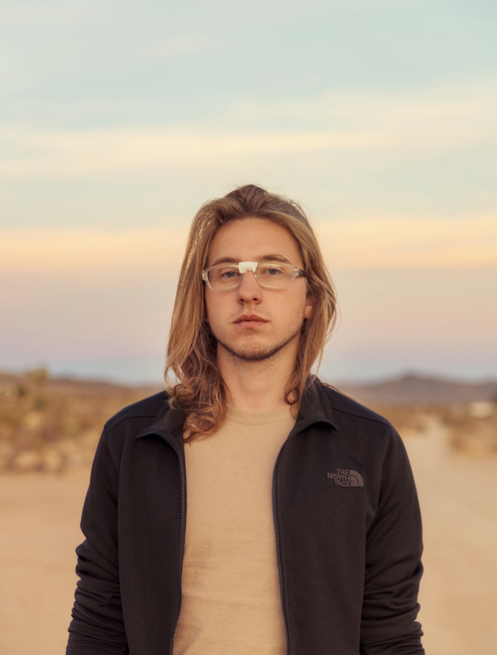 a man with long hair and glasses standing in the desert
