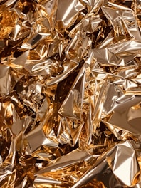 A close-up view of crumpled golden foil creating a textured, reflective surface with sharp creases and folds.