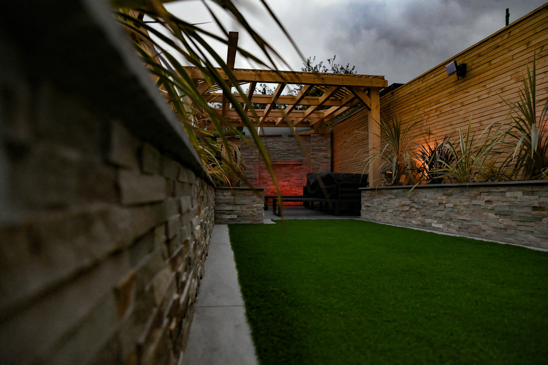 Stadstuin met houten pergola, natuurstenen muur en strak gazon