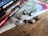 A collection of tabletop role-playing game manuals is stacked neatly on the left side. Next to them, a set of metallic polyhedral dice is arranged on a wooden table, with a colorful map-like cloth underneath.