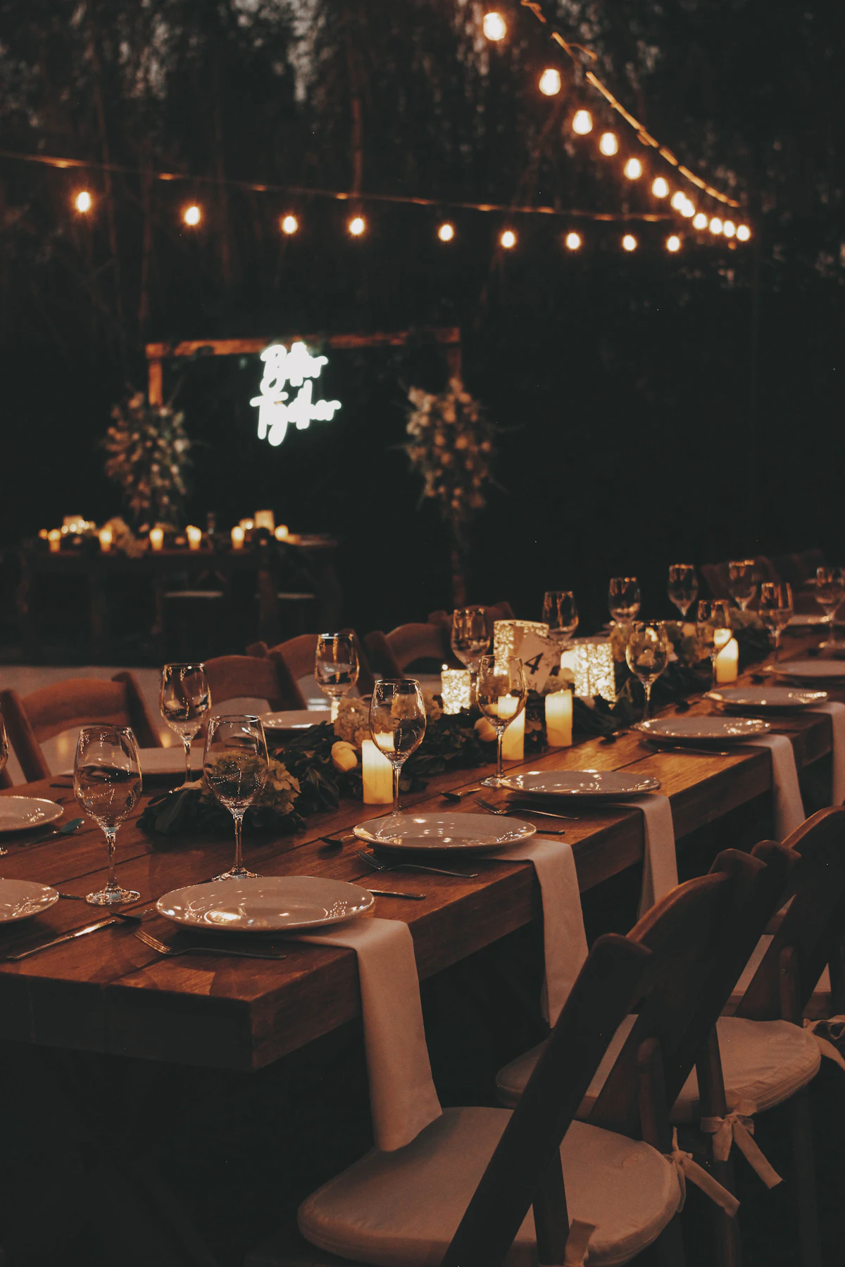 A long candlelit table laid for a dinner party in a dark room